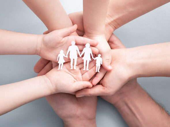 Hände einer Familie halten eine Scherenschnitt-Familie