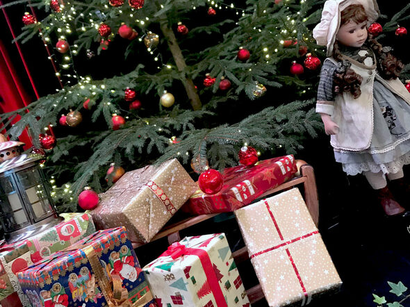 Ein geschmückter Weihnachtsbaum, davor Geschenke und eine Puppe