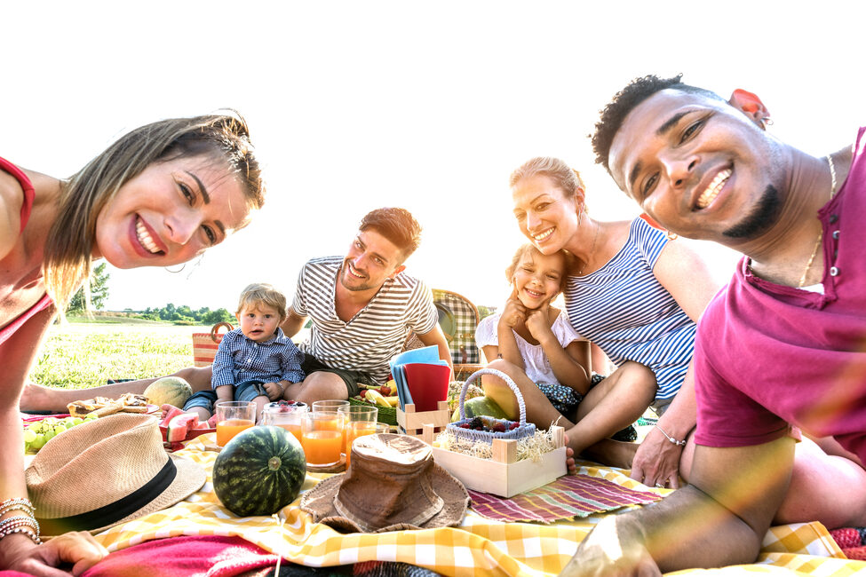 Eine Familie sitzt bei Sonnenschein auf einer Picknick-Decke.