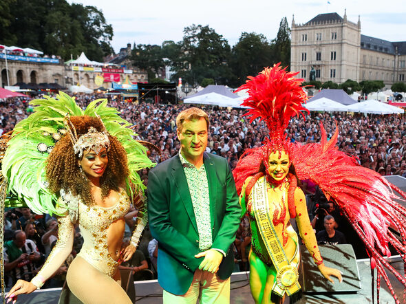 Ministerpräsident Markus Söder auf der Bühne des Sambafestivals, umringt von zwei Samba-Tänzerinnen
