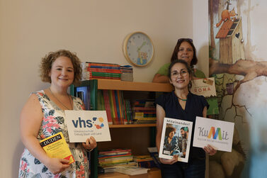 Laura Göldner und Helgard van Sein von der VHS Coburg vor dem neuen Bücherregal im Familienstützpunkt mit Leiterin Katja Fuß.