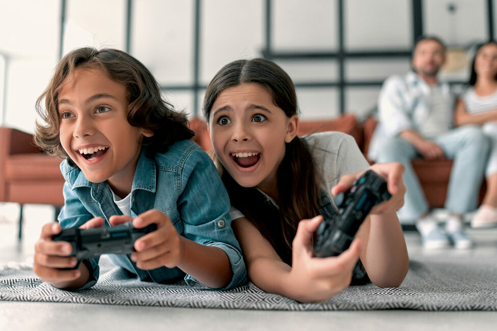 Spielende Kinder an der Spielkonsole mit Eltern im Hintergrund