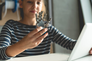 Ein Mädchen hält eine Roboterhand und ein Tablet in den Händen