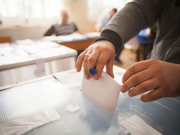 Eine Person wirft einen Stimmzettel in eine Wahlurne