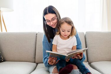 A,Happy,Kid,Sitting,On,Sofa,With,Babysitter,Holding,Book