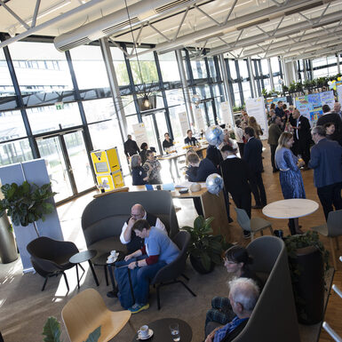 Mehrere Personen stehen in Gruppen an Stehtischen und unterhalten sich