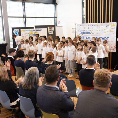 Publikum sitzt auf Stühlen. Vor ihnen steht ein Chor aus Schülerinnen und Schüler.