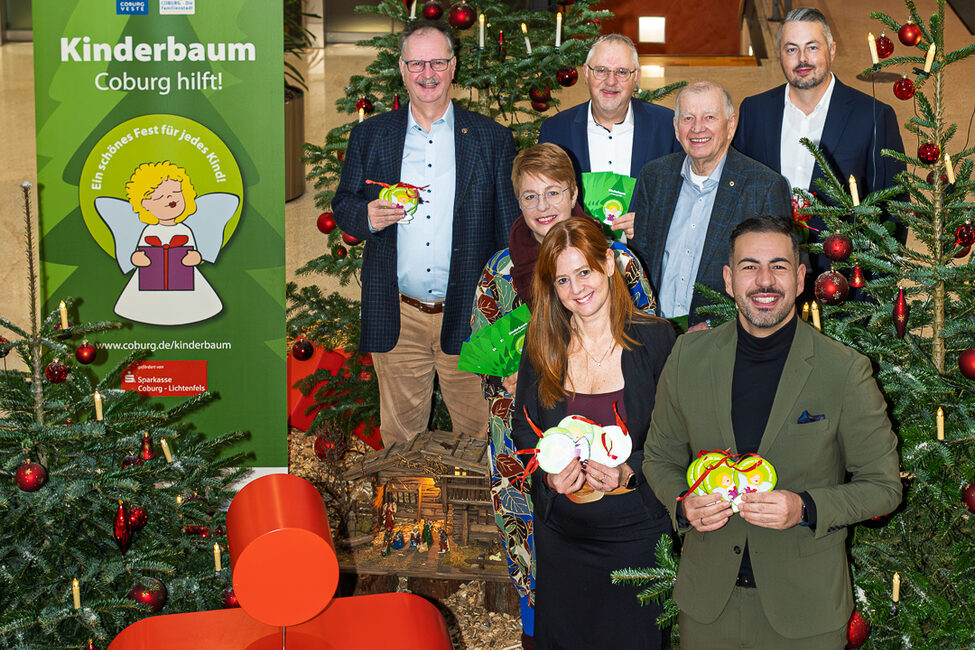 Sieben Personen stehen vor dem Wünschebaum der Kinder und freuen sich über die Aktion Kinderbaum