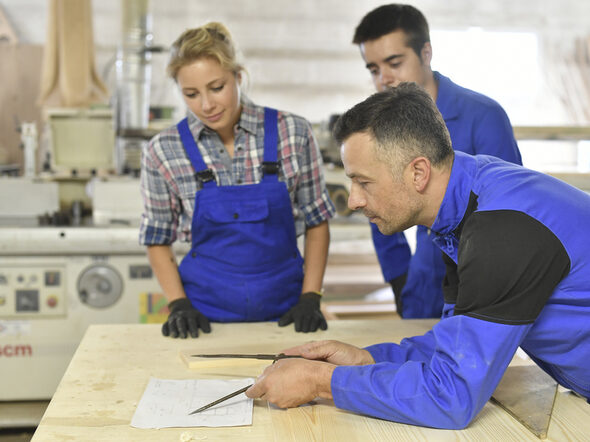 Ausbilder mit Zirkel erklärt zwei Auszubildenden einen Bauplan