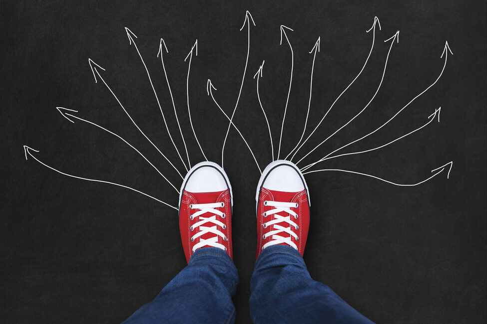 Viele Kreidepfeile führen von Füßen in roten Turnschuhen weg