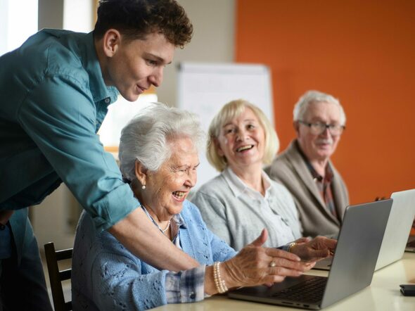 Jugendlicher hilft Senior*innen am Laptop