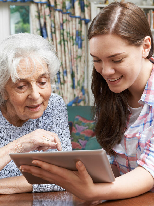 Jugendliche erklärt älterer Frau die Bedienung eines Tablet-Computers